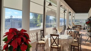 An outdoor dining area with tables and chairs, large windows, and a view of the city. - Hotel Valsequillo (Lepe)