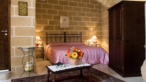 A cozy room with a stone wall, a bed with a pink bedspread, a wooden cabinet, and a small table with a vase of flowers. - Residenza de Leonardis (Alberobello)