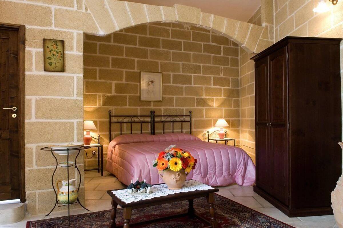 A cozy room with a stone wall, a bed with a pink bedspread, a wooden cabinet, and a small table with a vase of flowers.