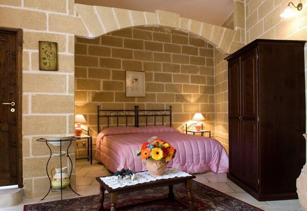 A cozy room with a stone wall, a bed with a pink bedspread, a wooden cabinet, and a small table with a vase of flowers.
