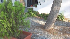 A building with a white exterior, a door, and a small porch area with potted plants and a tree. - Residenza de Leonardis (Alberobello)