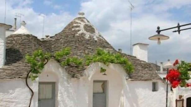 A traditional white building with a stone roof, potted plants, and a clear sky. - Residenza de Leonardis (Alberobello)