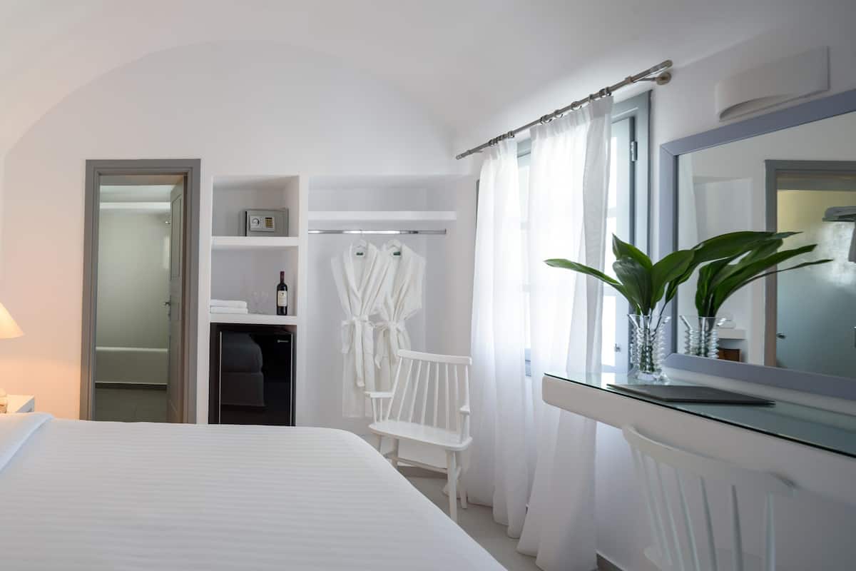 A hotel room with a bed, a bedside lamp, a mirror, a window with curtains, and a potted plant.