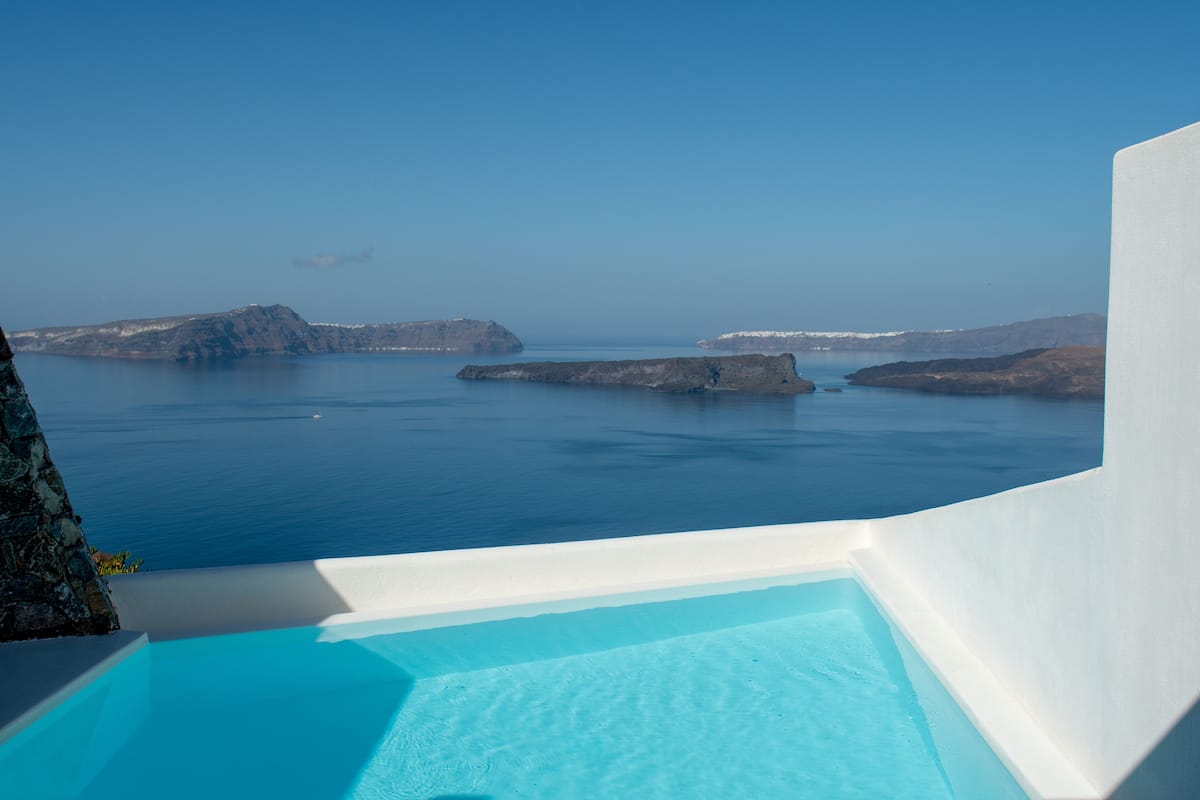 A clear view of a swimming pool with a white edge, overlooking a calm sea and rocky islands.
