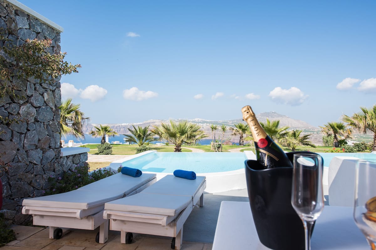 A poolside area with lounge chairs, a bottle of champagne, and a glass of wine.