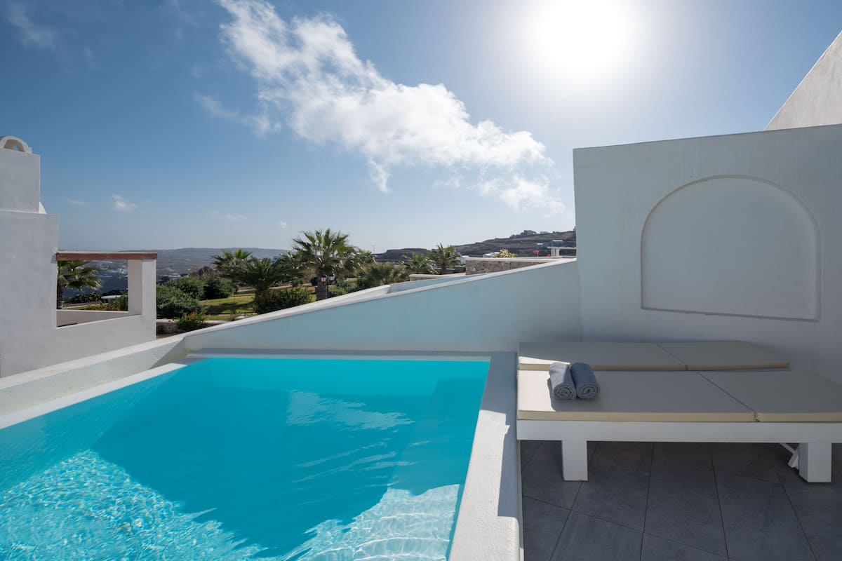 A rooftop pool with clear blue water, a white lounge area, and a view of the landscape and distant buildings.