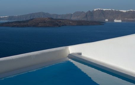 A clear view of a swimming pool with a white edge, a calm blue sea, and a distant island with mountains.