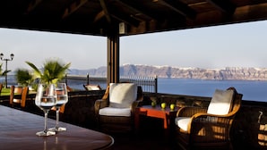An outdoor seating area with wicker chairs and a table, overlooking a coastal landscape. - Maison Des Lys (Santorini)