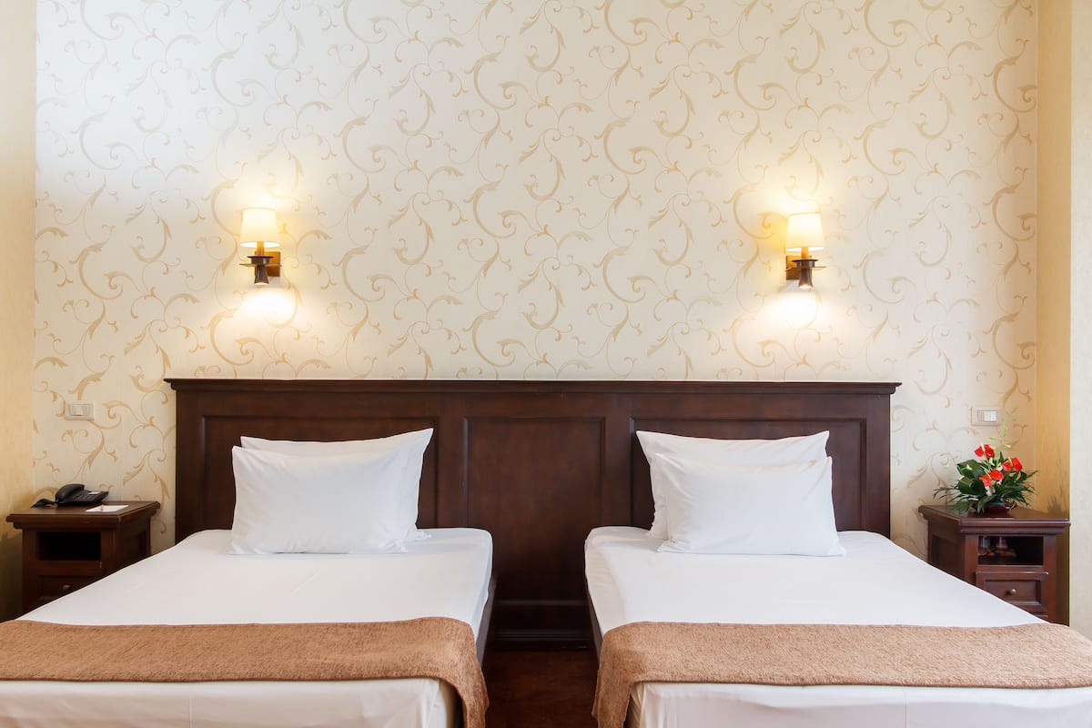 Habitación de hotel con dos camas, cabecera de madera, mesita de noche con teléfono y una pared con diseño decorativo.