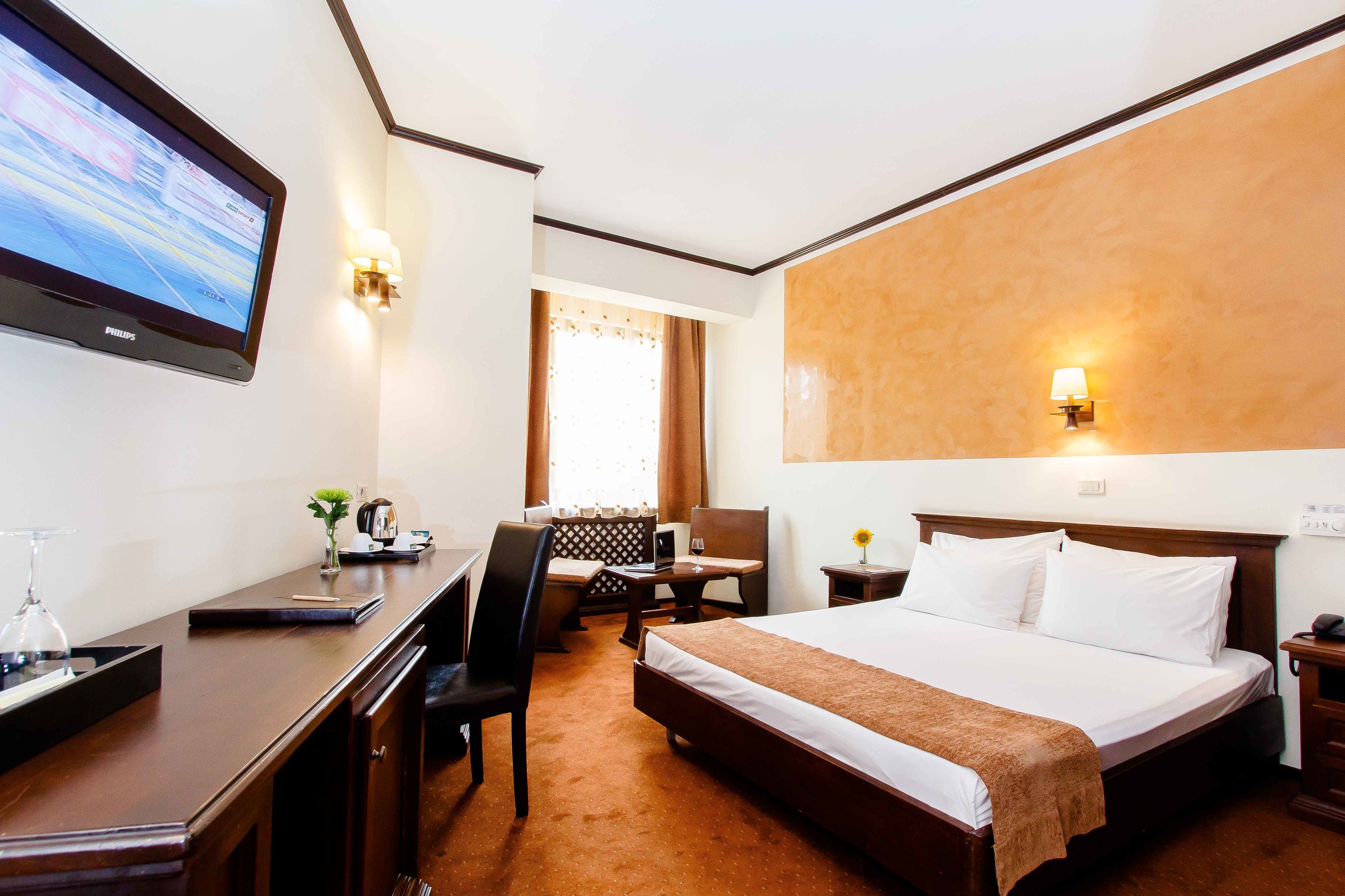 A hotel room with a bed, desk, chair, and a TV mounted on the wall.