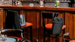 Baaritiskialue, jossa on puupanelointi, baaritiskin yläpuolella oleva televisio sekä erilaisia alkoholijuomapulloja. Alueella on oranssit tuolit ja pöytä, jonka päällä on lasi ja kukka.