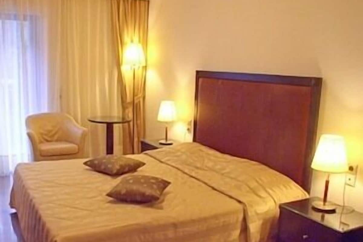 Una habitación de hotel con una cama grande, dos lámparas de noche, una silla y una mesita de noche.