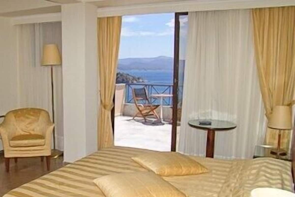 Habitación de hotel con una cama, una silla, una mesita y vista al mar.