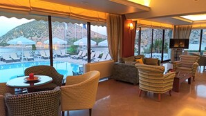 A spacious lounge area with a pool view, comfortable seating, and a flat-screen TV. - King Minos (Nafplio)