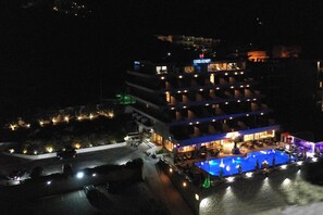 A multi-story hotel with a pool area, outdoor lighting, and a sign indicating a restaurant. - King Minos (Nafplio)