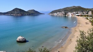 A coastal town with a sandy beach, clear blue waters, and hills in the background. - King Minos (Nafplio)