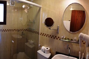 Un baño con cabina de ducha de vidrio, inodoro, lavamanos, espejo y secador de pelo.