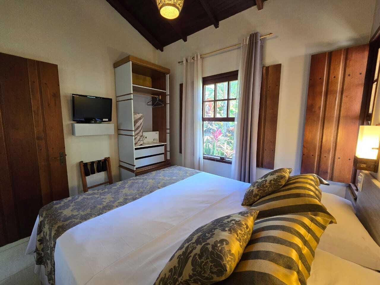 A bedroom with a large bed, a TV mounted on the wall, a wardrobe, and a window with curtains.