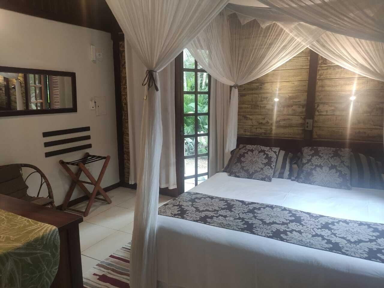 Un dormitorio con cama a dosel, cabecera de madera, una mesita y una silla.