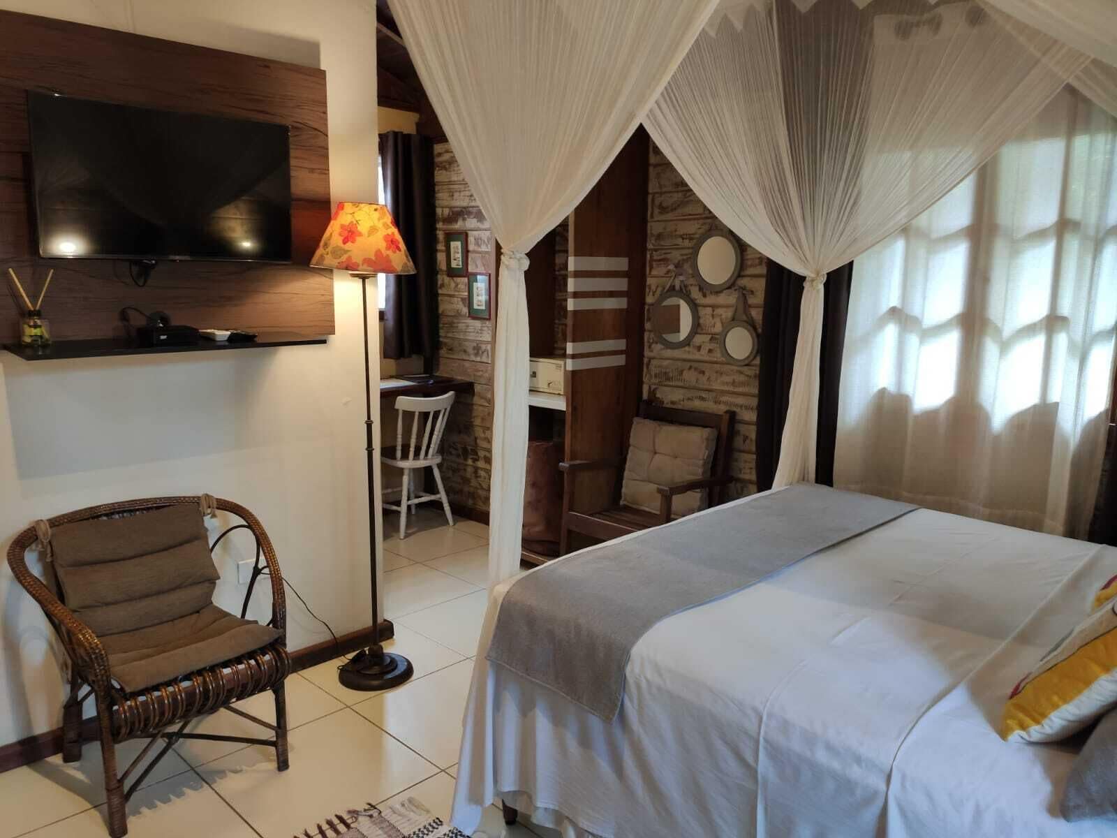 Un dormitorio con cama, televisor, lámpara, silla y escritorio.