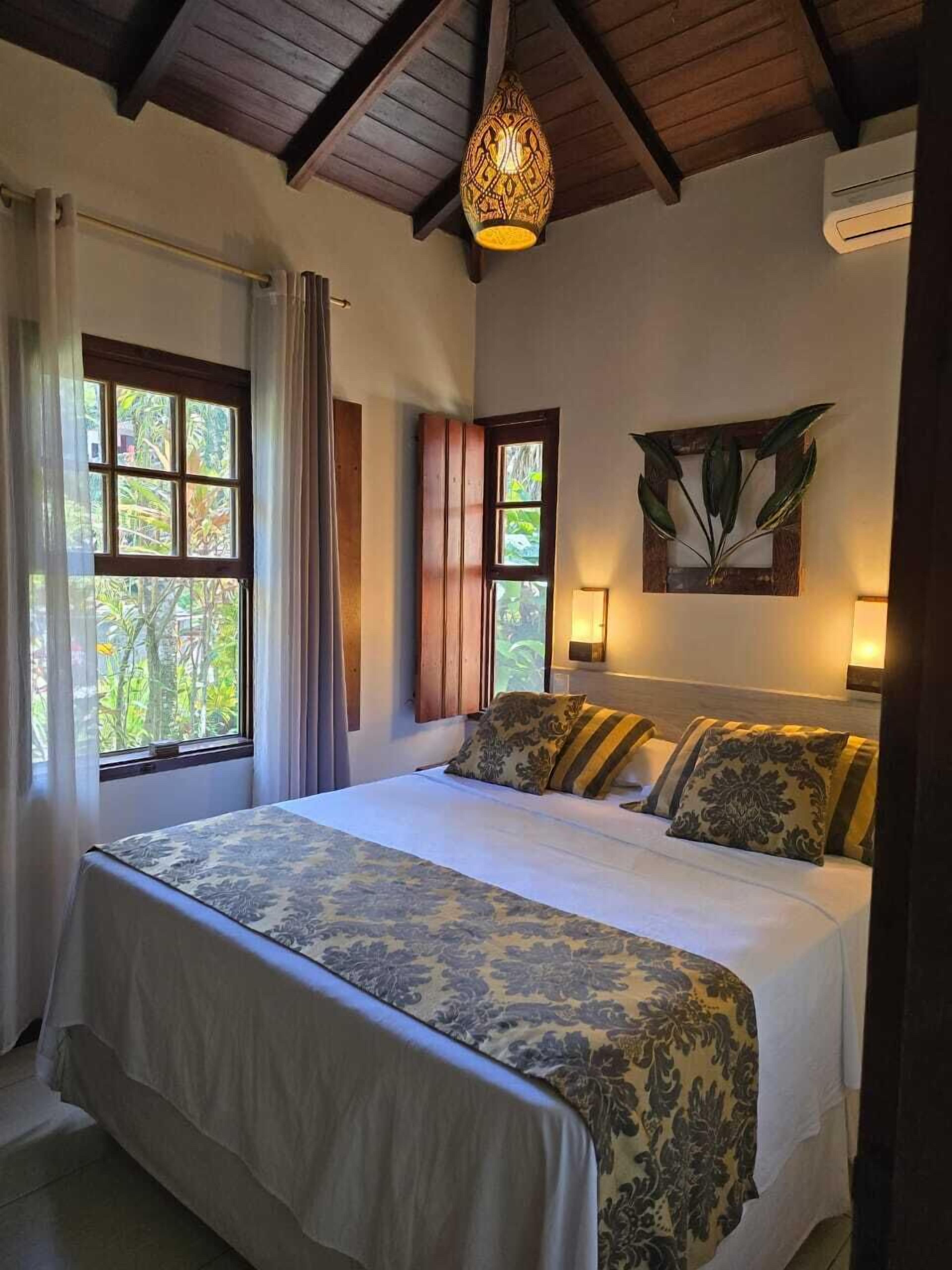 A bedroom with a large bed, a ceiling fan, a window with curtains, and a wall-mounted light fixture.