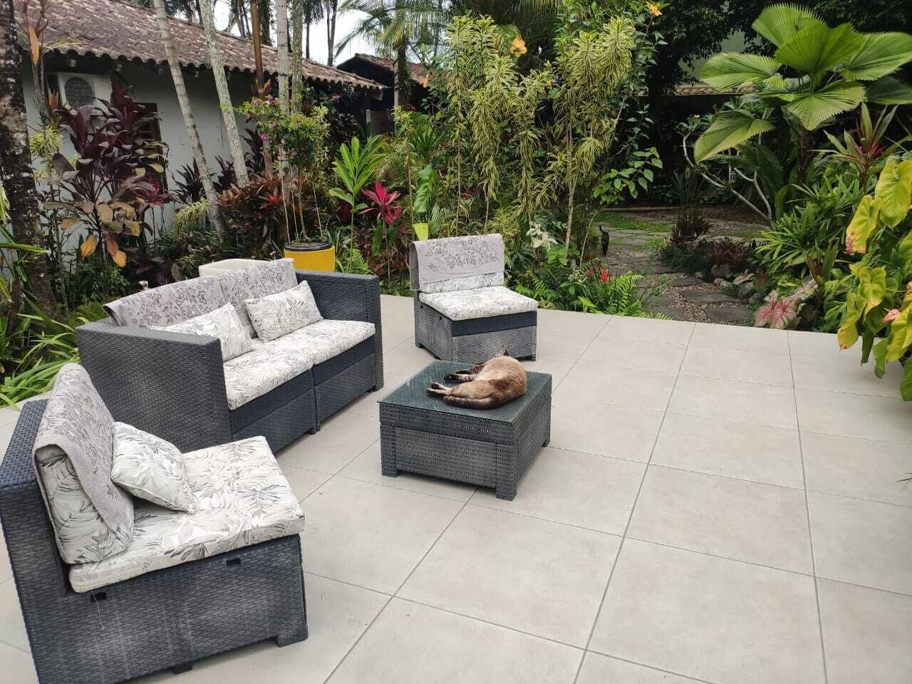 An outdoor seating area with wicker furniture and a small table, surrounded by lush tropical plants.