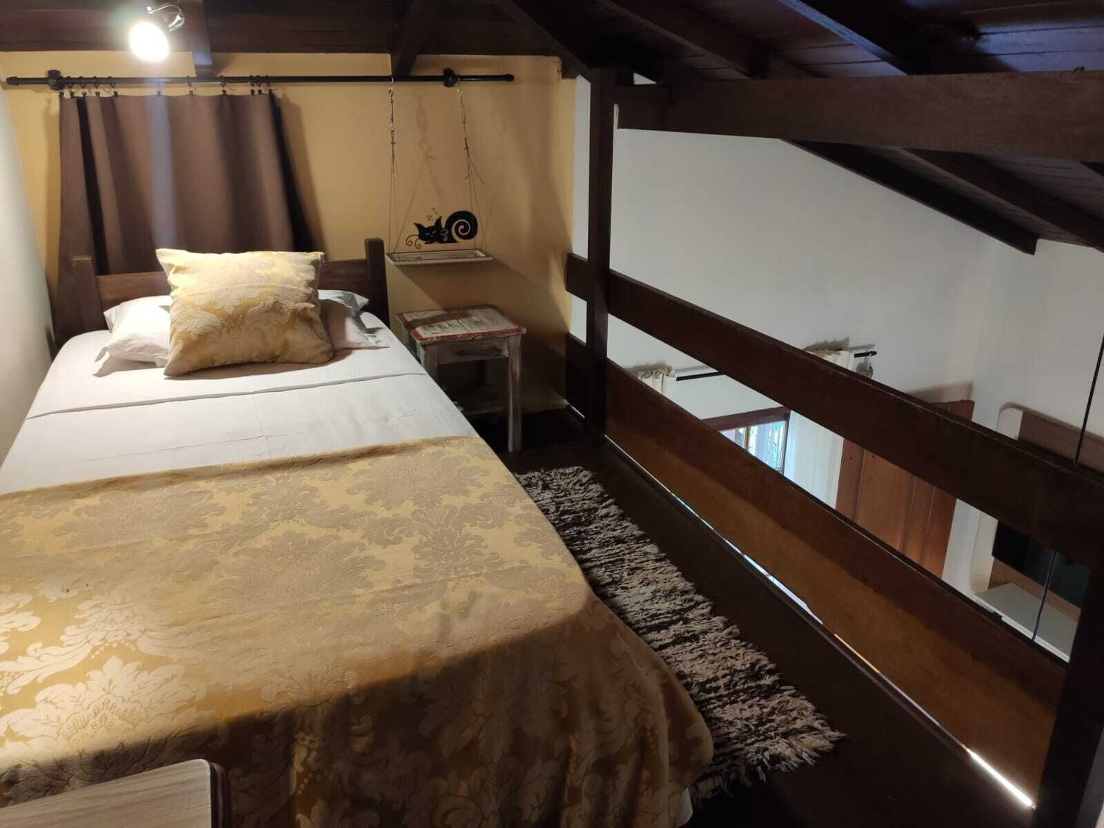 A bedroom with a bed, a small bedside table, a hanging chair, and a view of the outside.