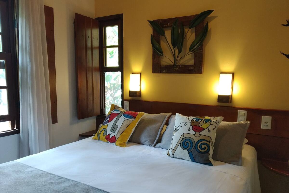 A hotel room with a bed, two wall-mounted lights, a window with curtains, and a wall-mounted plant.