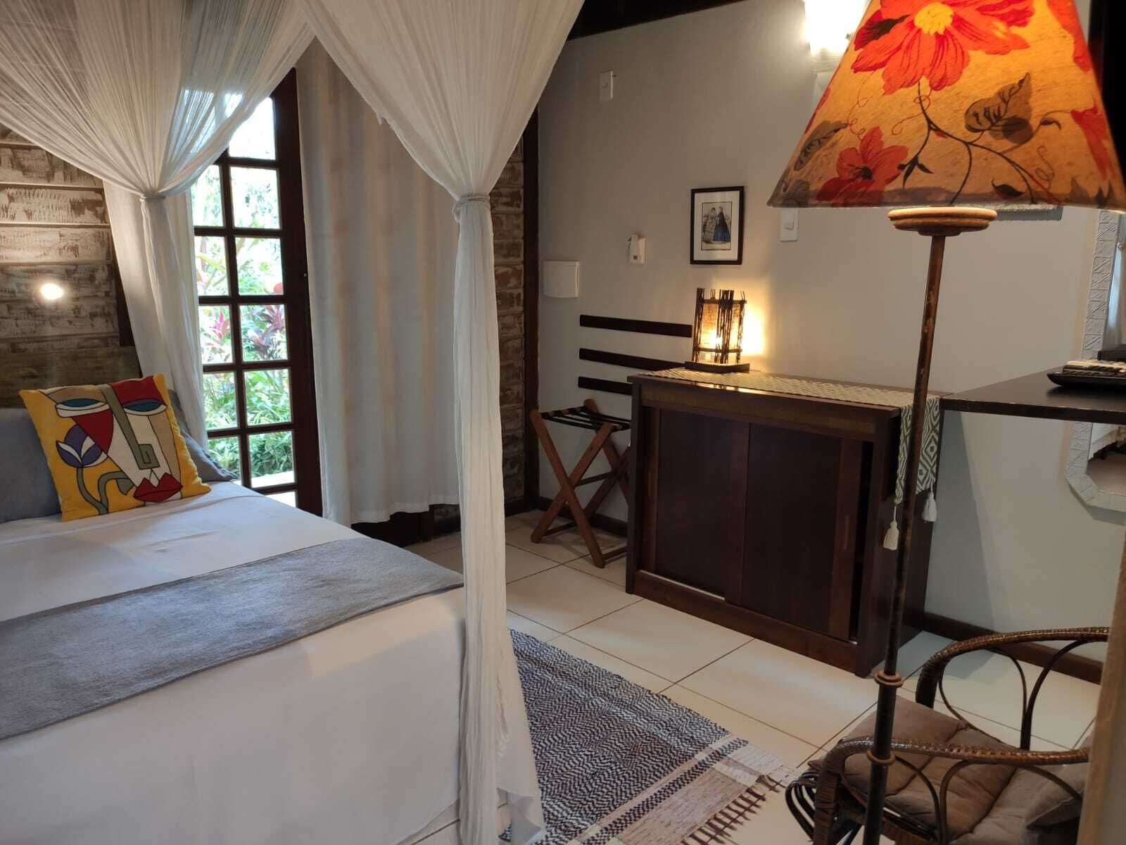 A bedroom with a bed, a bedside table, a lamp, a chair, and a window with curtains.