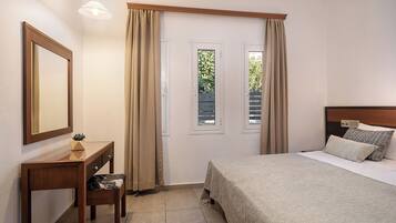 Un dormitorio con cama, escritorio con silla, espejo y dos ventanas con cortinas.
