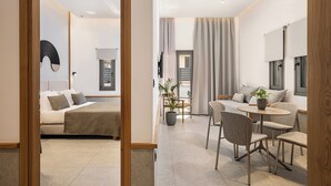 Una habitación de hotel moderna con cama, zona de estar con mesa y sillas, y un espejo grande.