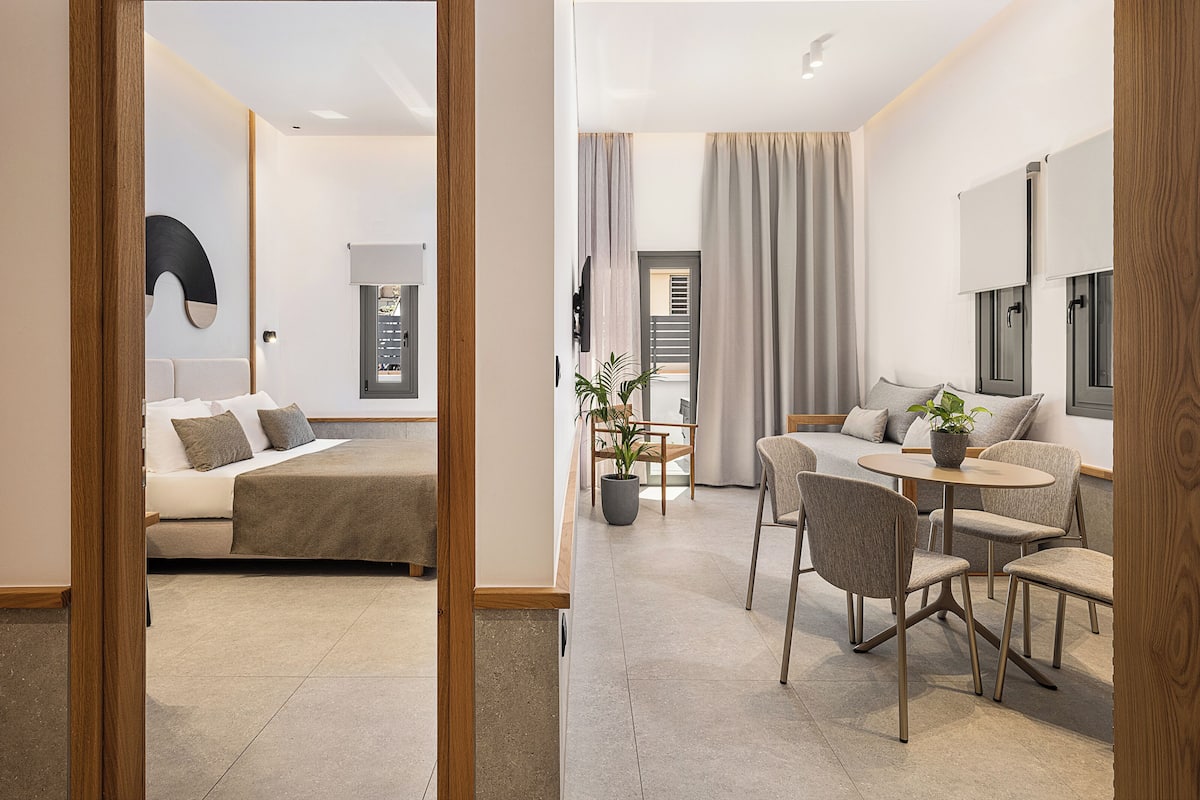 A modern hotel room with a bed, a seating area with a table and chairs, and a large mirror.
