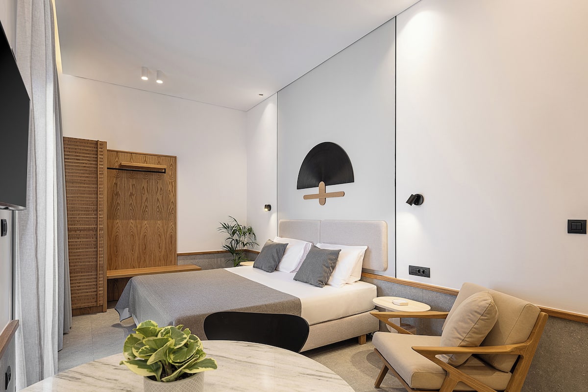 A modern bedroom with a bed, bedside table, chair, and a potted plant.