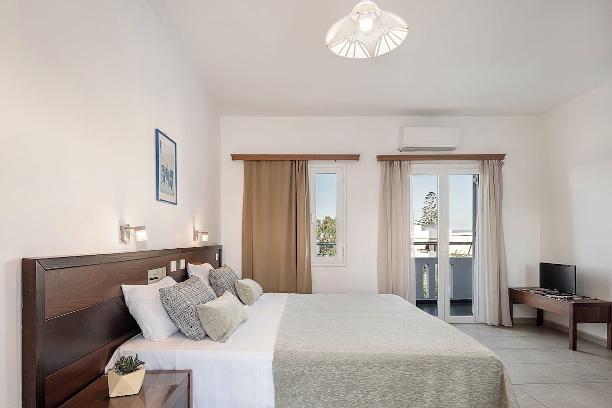 A hotel room with a large bed, bedside tables, a TV, and an air conditioning unit.