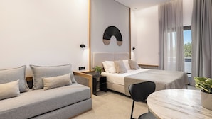Una habitación de hotel moderna con sofá, cama, mesa de comedor y vistas al exterior.
