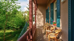 A balcony with wicker chairs and a table, overlooking a lush garden and trees. - Ábel Pension Budapest (Budapest)