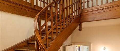 A wooden spiral staircase with a handrail, leading to an upper floor.