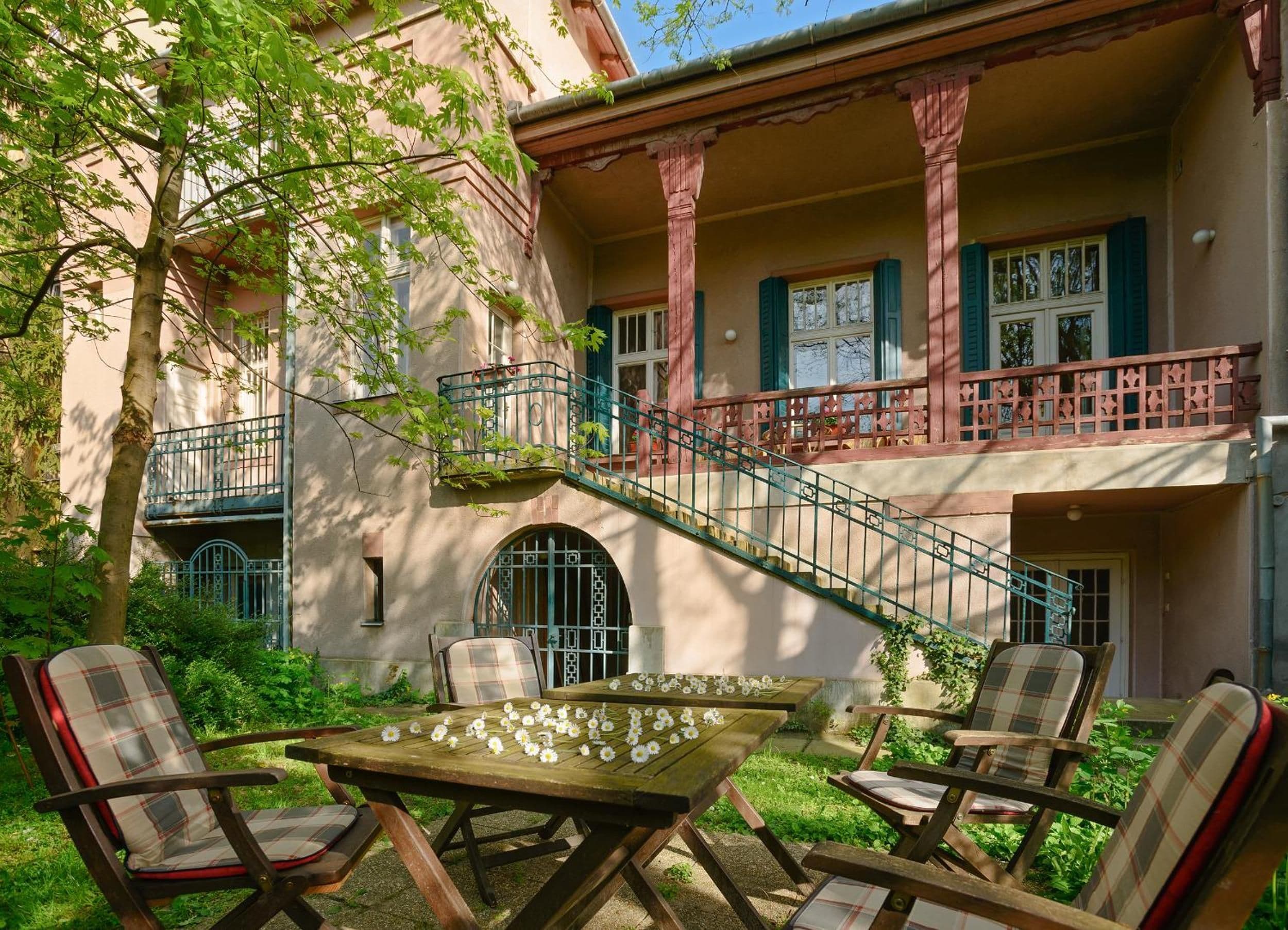 A building with a balcony, a staircase, and outdoor seating with flowers.
