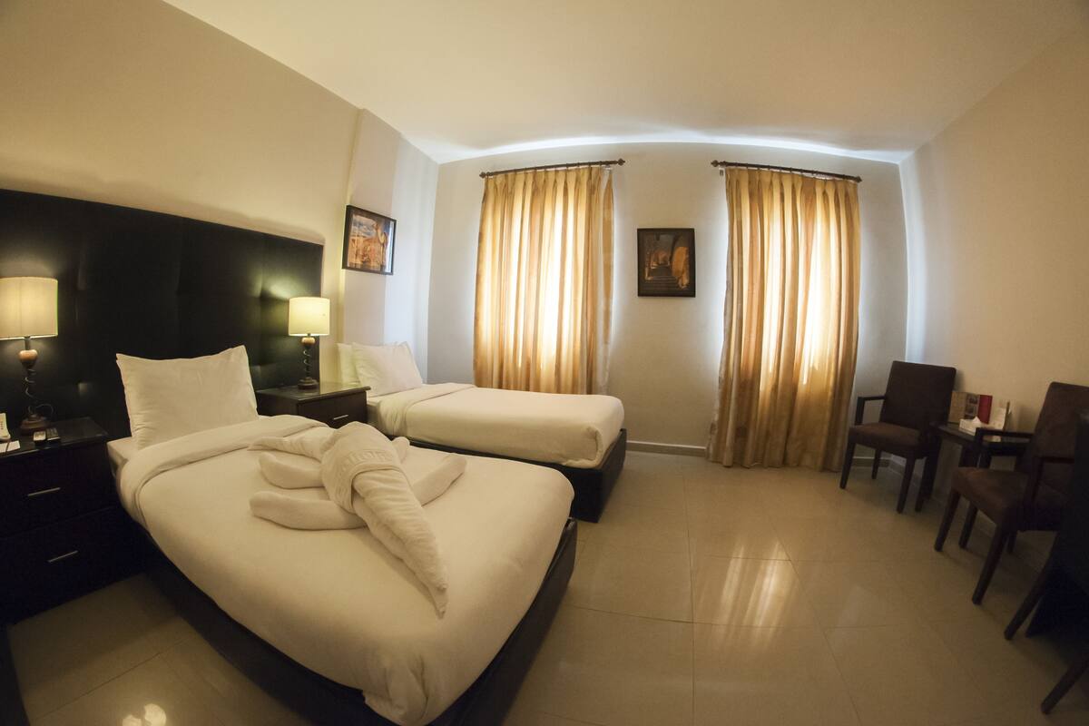 A hotel room with two beds, a desk, a chair, and curtains.