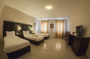 Habitación de hotel con dos camas, un escritorio, televisor y cortinas.