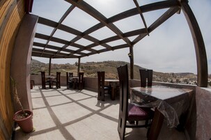 Un patio al aire libre con mobiliario de madera y vistas a un paisaje montañoso.