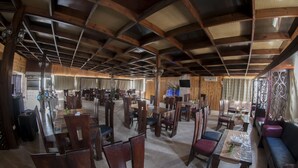 A spacious dining area with wooden tables and chairs, a high ceiling with wooden beams, and a large window providing natural light. - La Maison Hotel Petra (Wadi Musa)