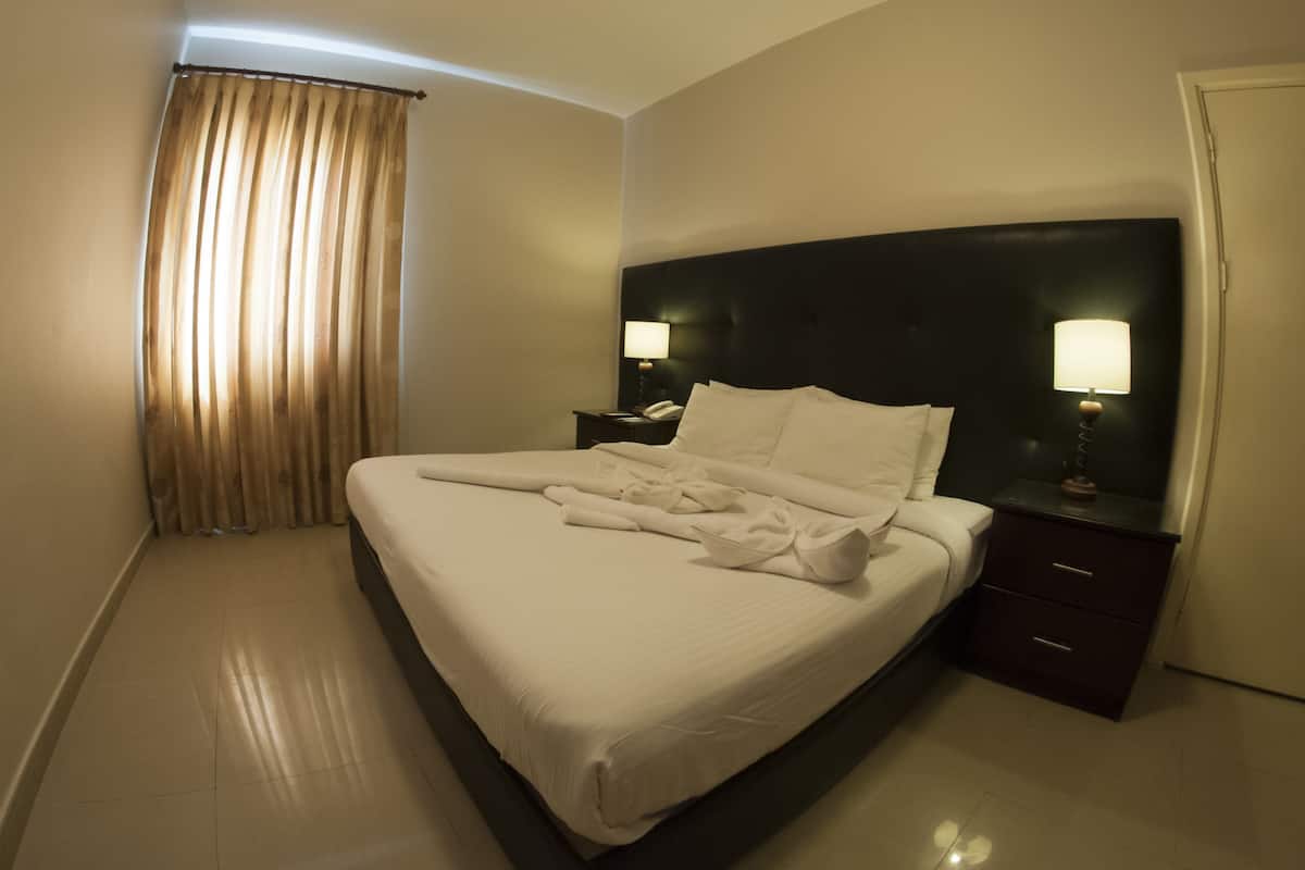 A hotel room with a neatly made bed, two bedside tables with lamps, a dark headboard, and a door on the right.