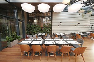 Un comedor moderno con mesas dispuestas para varias personas, sillas de madera y lámparas colgantes.