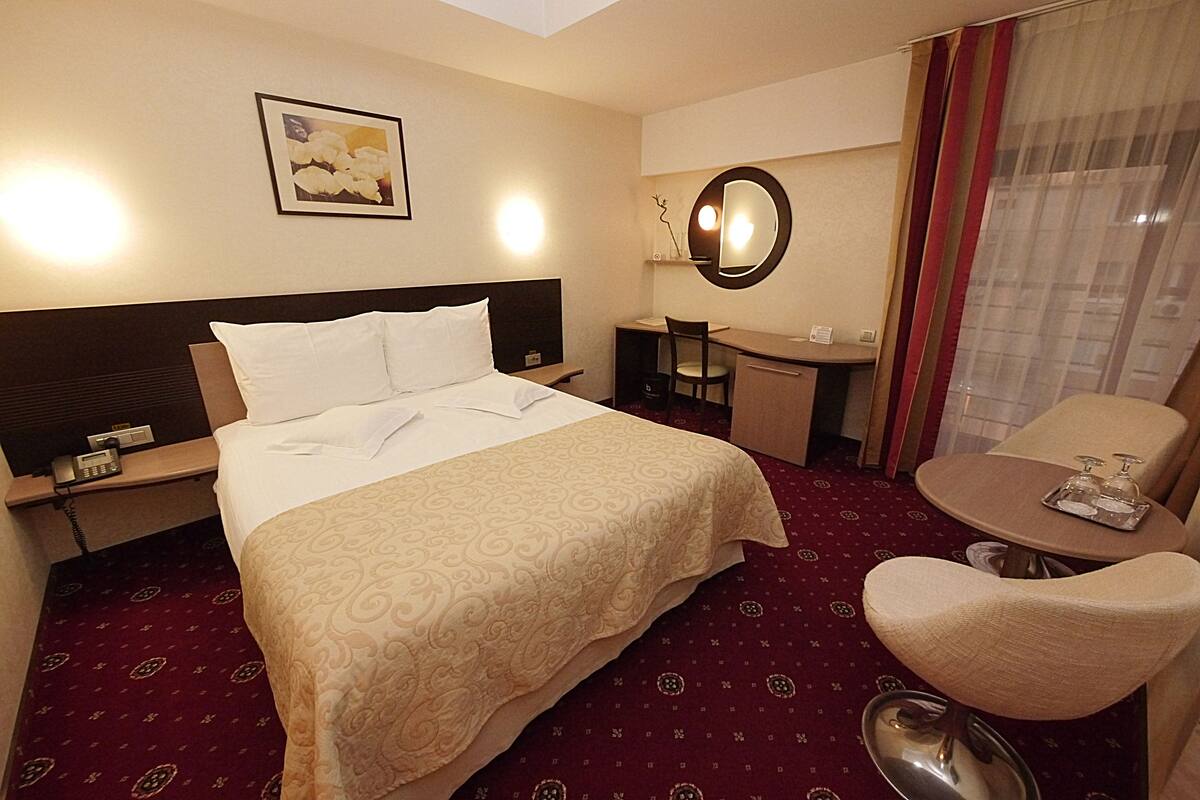 Habitación de hotel con cama, escritorio, silla y una mesita con detalles de cortesía.