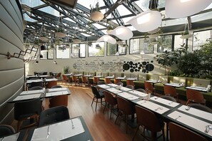 Un restaurant spacieux avec de hauts plafonds, de grandes fenêtres et différents types de sièges, notamment des banquettes et des tables.