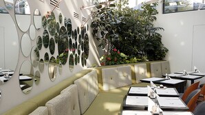 Un restaurante con una zona de estar con asientos verdes, varias mesas con menús y una pared decorada con espejos.
