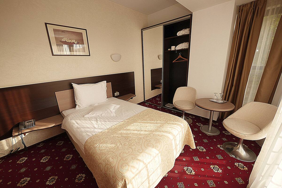 Una habitación de hotel con cama, mesita de noche, silla y una pequeña mesa redonda.