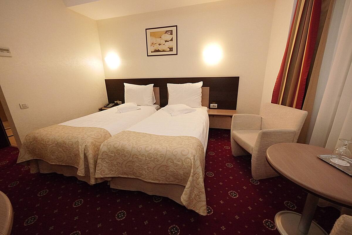 Habitación de hotel con dos camas, una silla, una mesita pequeña y un cuadro colgado en la pared.
