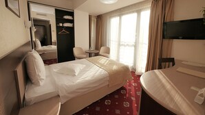 Habitación de hotel con una cama, escritorio, silla, televisión y baño visible a través de una puerta abierta.